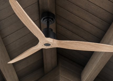 A three-blade ceiling fan with light natural wood blades and a matte black motor housing, shown installed on a dark wood-beamed ceiling.